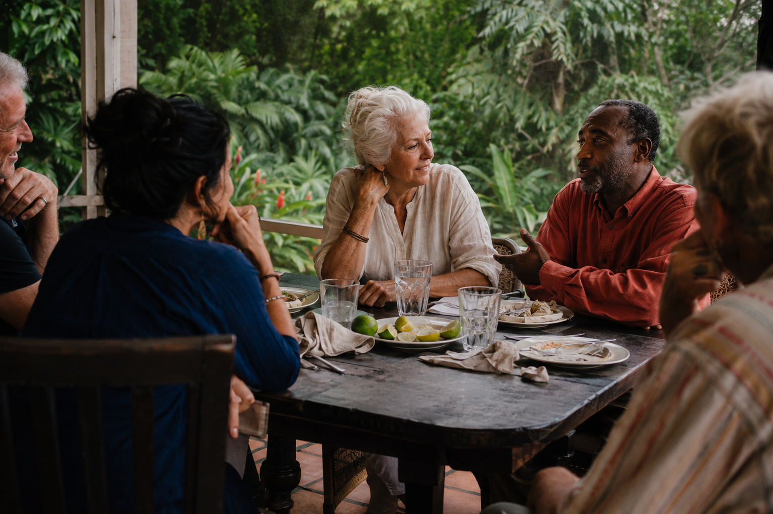 People of different ages talking around a veranda table in warm afternoon light.